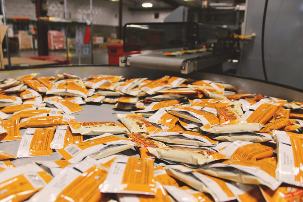 Many individually wrapped BumbleBar bars spread across a stainless steel rotary accumulation table.