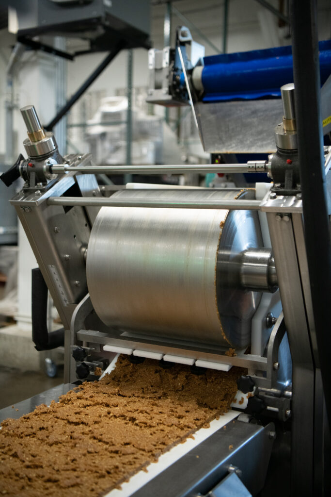 Commercial dough sheeting machine pressing a continuous sheet of bar product onto a conveyor