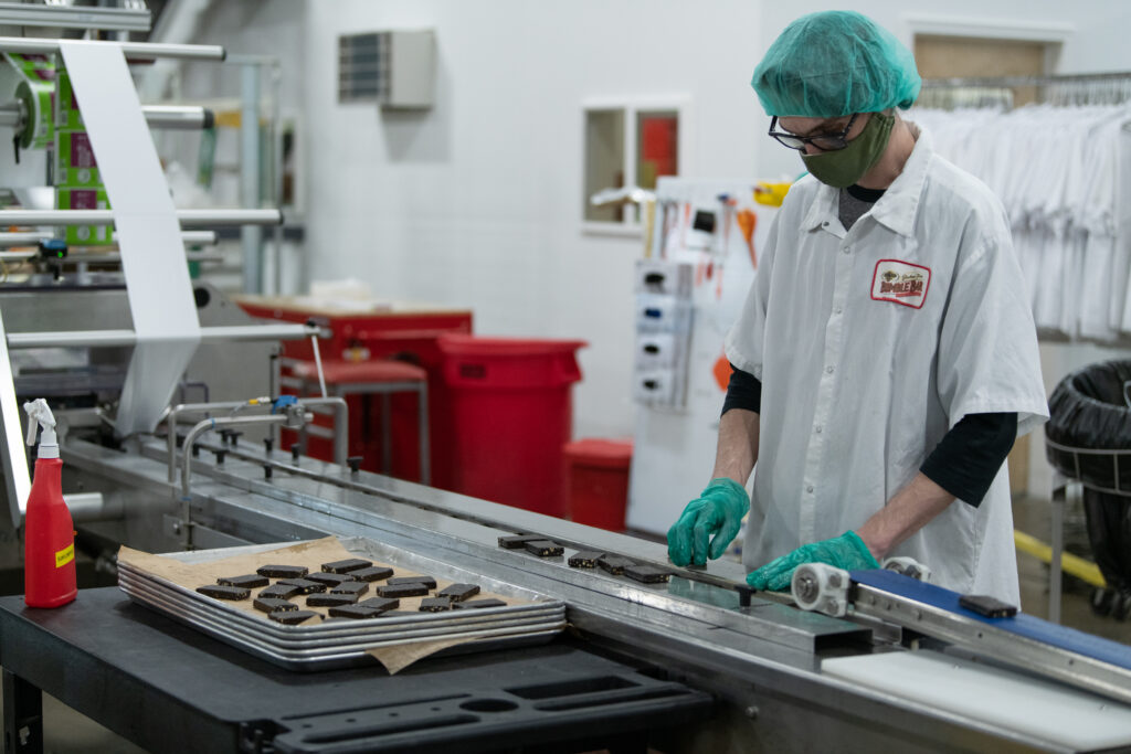 Food production worker in a hairnet feeding bars onto a conveyor line in a manufacturing facility