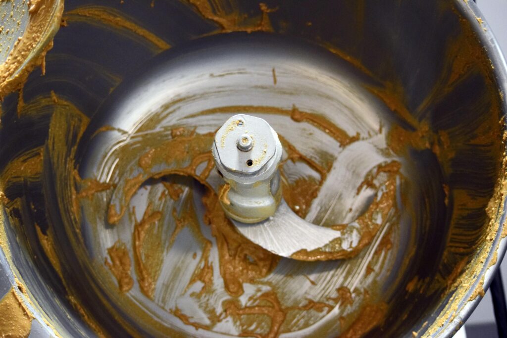 Fresh peanut butter inside an industrial grinder bowl with the blade visible