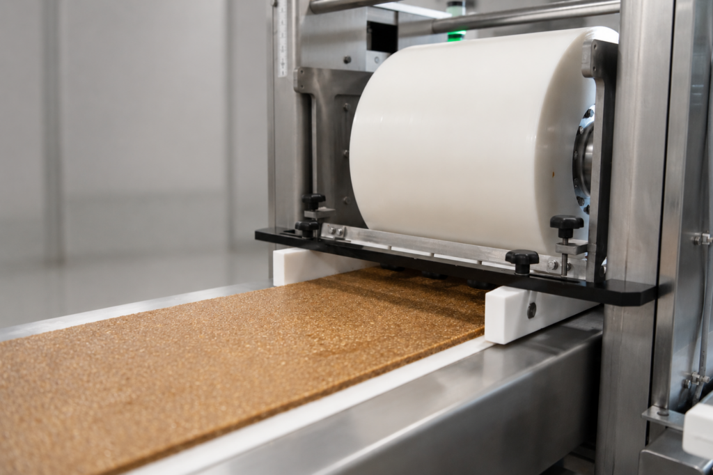 Commercial flow-wrapper machine feeding a roll of packaging film over a slab of bar product on a conveyor