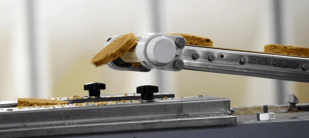 Closeup of a bar puck on a conveyor belt with a mechanical guide arm.