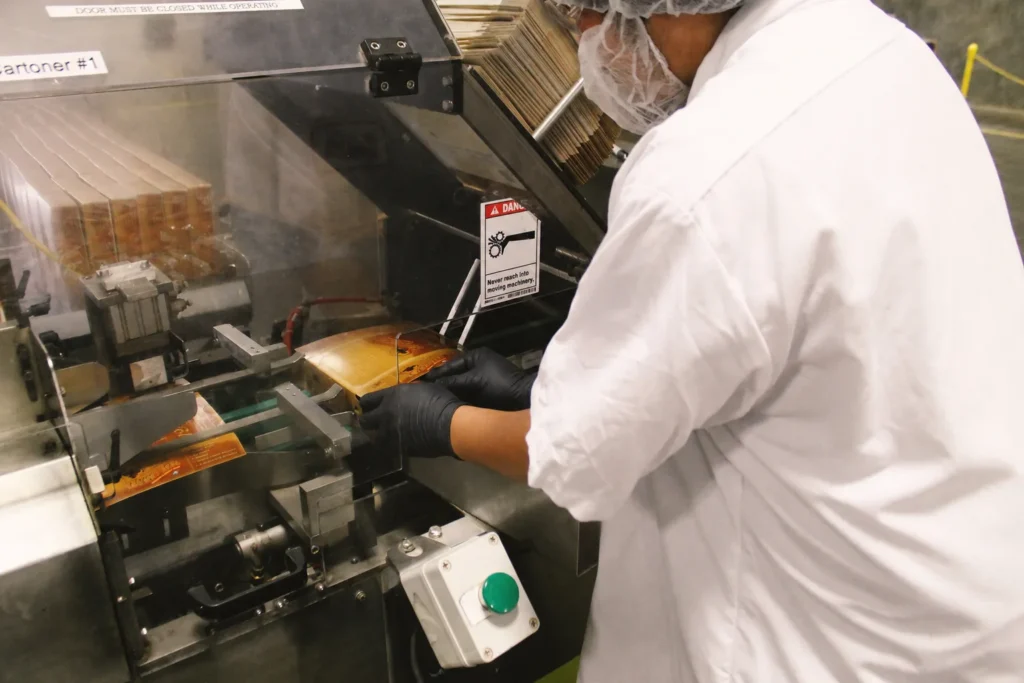 A factory worker cartoning BumbleBar bars on the production line — the kind of operation behind our food product recall story.